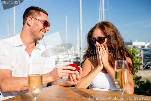 Image of smiling couple with champagne and gift at cafe