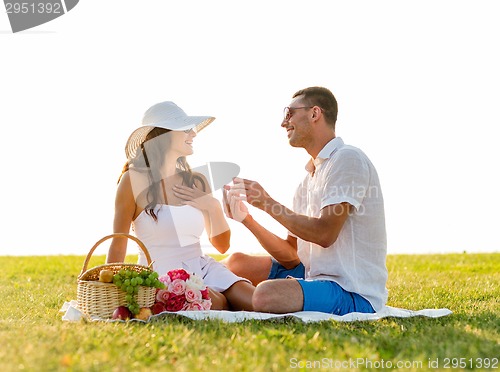Image of smiling couple with small red gift box on picnic