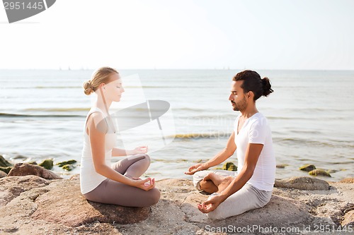 Image of smiling couple making yoga exercises outdoors