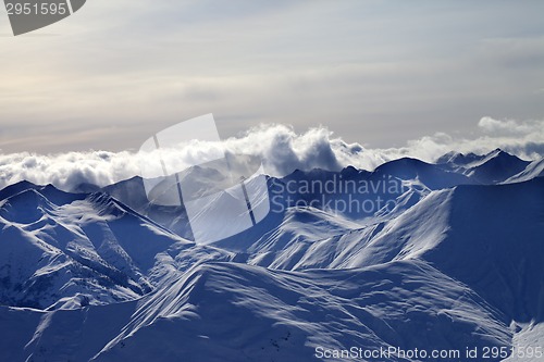 Image of Evening snowy mountains in mist and sunlight clouds