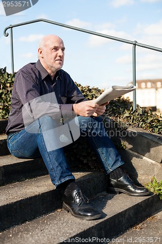 Image of Man sitting on steps reading a newspaper