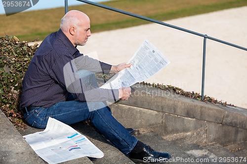 Image of Man sitting on steps reading a newspaper