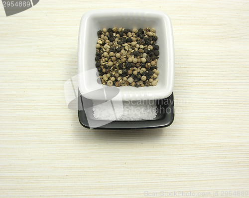 Image of Bowls of chinaware with peppercorns and salt on beige underlay