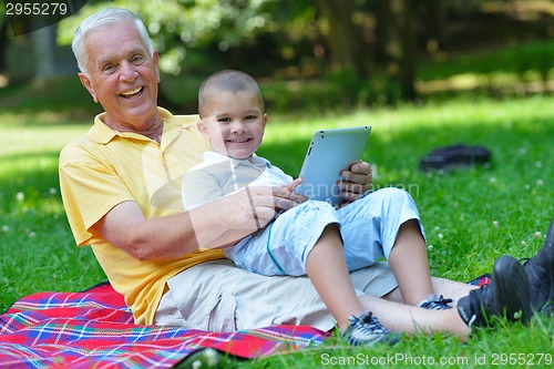 Image of grandfather and child in park using tablet