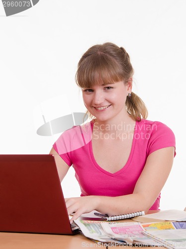 Image of Girl with laptop and newspaper sitting at table