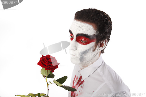 Image of Man with white mascara and bloody shirt holds red rose