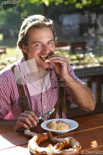 Image of Attractive man eats traditional cheese with pretzel in a Bavaria