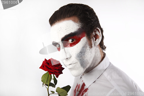 Image of Man with white mascara and bloody shirt holds red rose