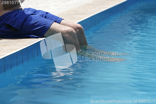 Image of Attractive man with blue swimsuit sitting on the edge of the poo