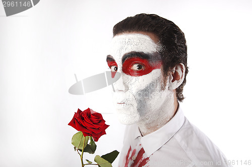 Image of Man with white mascara and bloody shirt holds red rose