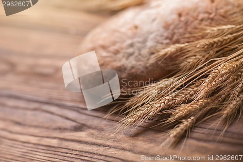 Image of wheat and bread on wooden table, shallow DOF