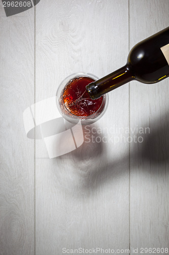 Image of Red wine pouring into glass from bottle on white wooden table. T