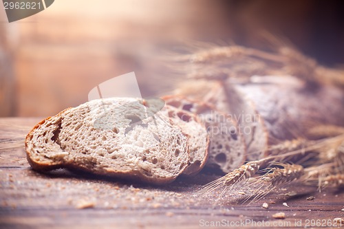 Image of Bread and wheat on wooden table, shallow DOF