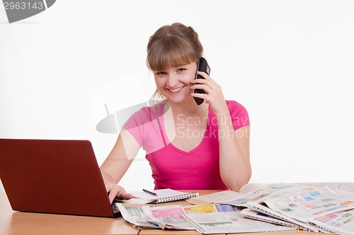 Image of Girl talking on phone while sitting at a table with laptop