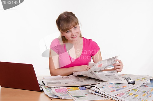 Image of girl thumbs through a newspaper while sitting at table