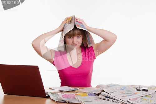 Image of The girl at the table with a newspaper on his head