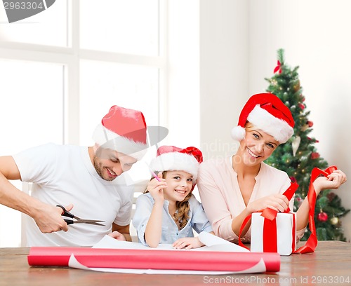 Image of happy family in santa helper hats packing gift