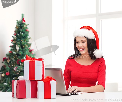 Image of smiling woman in santa hat with gifts and laptop