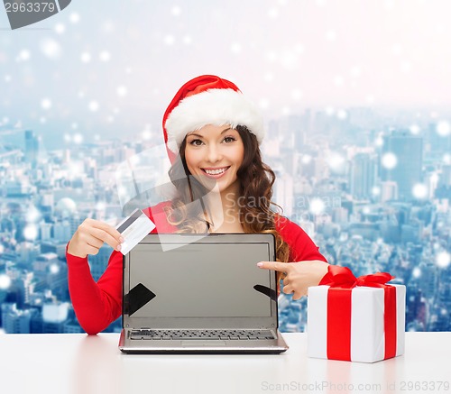 Image of smiling woman in santa hat with gift and laptop