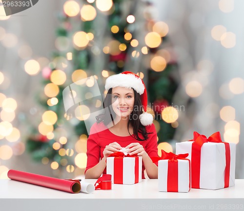 Image of smiling woman in santa helper hat packing gifts