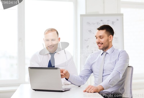 Image of two smiling businessmen with laptop in office