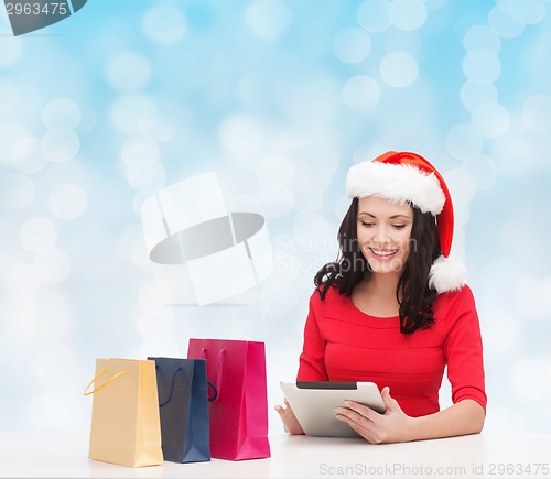 Image of smiling woman in santa hat with bags and tablet pc