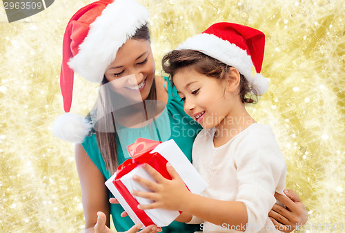 Image of happy mother and girl in santa hats with gift box