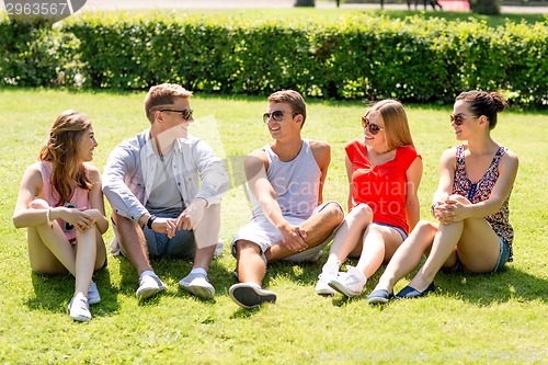 Image of group of smiling friends outdoors sitting on grass