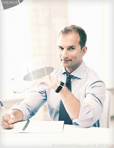 Image of businessman with spectacles writing in notebook