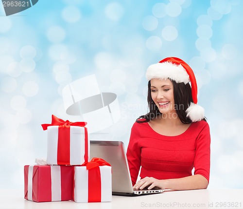 Image of smiling woman in santa hat with gifts and laptop