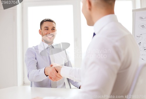 Image of two smiling businessmen shaking hands in office