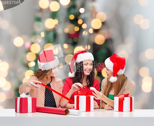 Image of smiling women in santa helper hats packing gifts