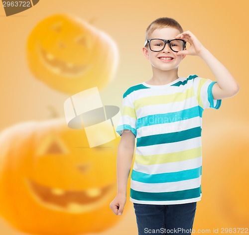 Image of smiling boy in glasses over pumpkins background