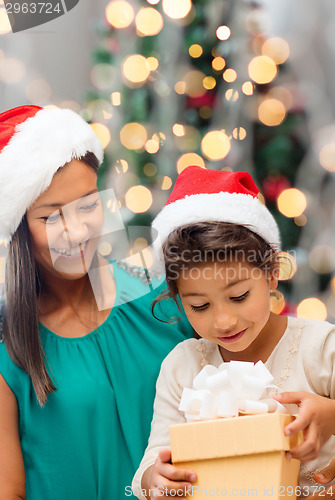 Image of happy mother and girl in santa hats with gift box