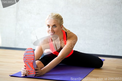 Image of smiling woman doing exercises on mat in gym