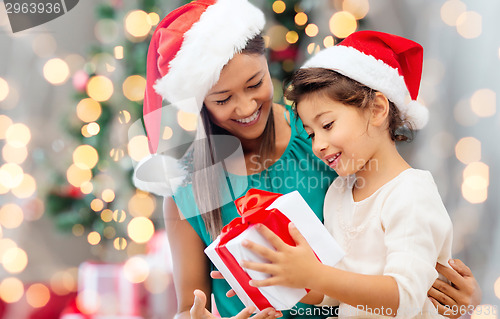 Image of happy mother and girl in santa hats with gift box