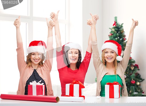 Image of smiling women in santa helper hats packing gifts
