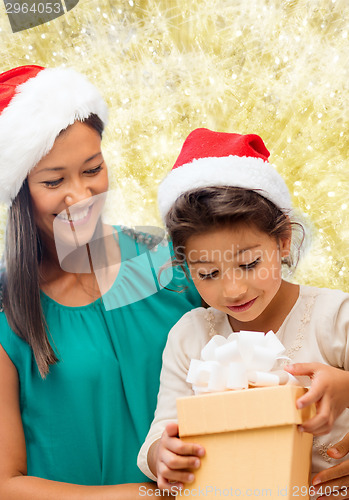 Image of happy mother and girl in santa hats with gift box