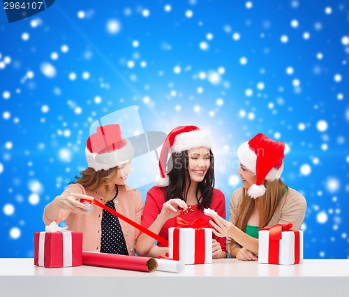Image of smiling women in santa helper hats packing gifts