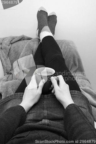 Image of Woman holding a hot drink, relaxing with her feet up