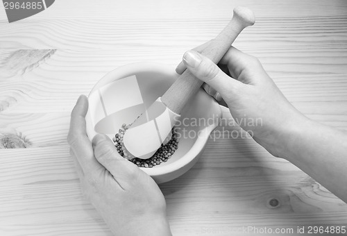Image of Two hands holding a pestle and mortar with whole coriander seeds