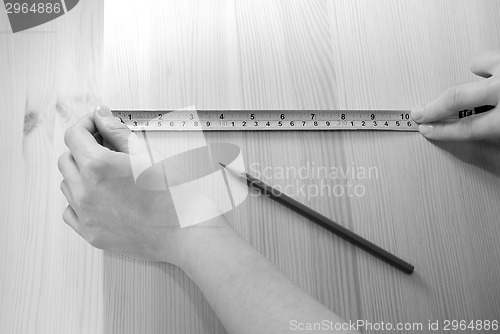 Image of Two hands measure a wooden board with a steel tape measure