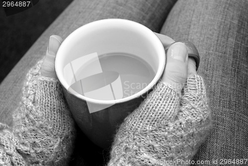 Image of A woman in a cosy jumper holds a cup of tea or coffee on her lap