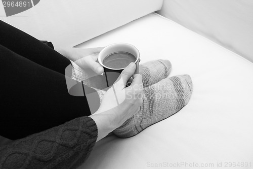 Image of Woman's hands holding a hot beverage, sitting on a couch