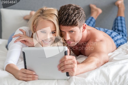 Image of Young couple reading a tablet in bed