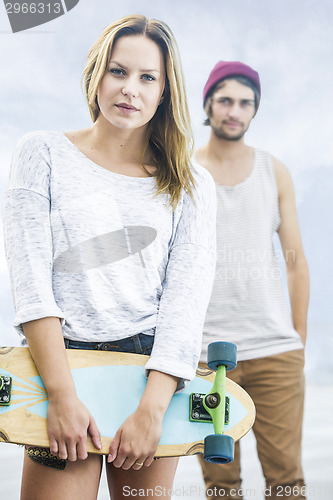 Image of girl with a skateboard stands in front of a boy