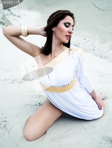 Image of Young pretty woman in greek tunic on sand