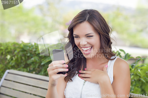 Image of Smiling Young Adult Female Texting on Cell Phone Outdoors