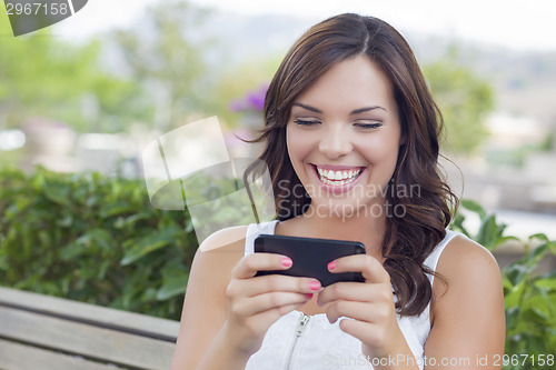 Image of Smiling Young Adult Female Texting on Cell Phone Outdoors