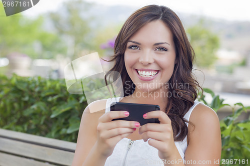 Image of Smiling Young Adult Female Texting on Cell Phone Outdoors